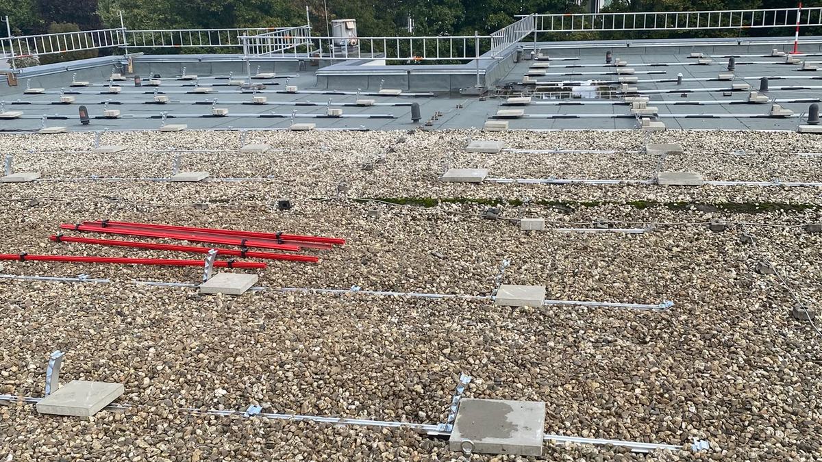 Aluminiumschienen und Betonplatten liegen als Unterkonstruktion auf der Kiesfläche des Flachdachs, noch ohne Module
